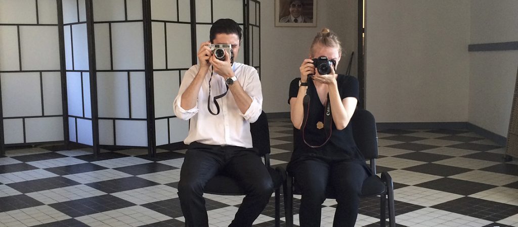 Deux photographes, un homme et une femme, sont entrein de prendre en photo la personne qui le sphotographie. le sol en damier noir et blanc réhausse la mise en abime de l'image