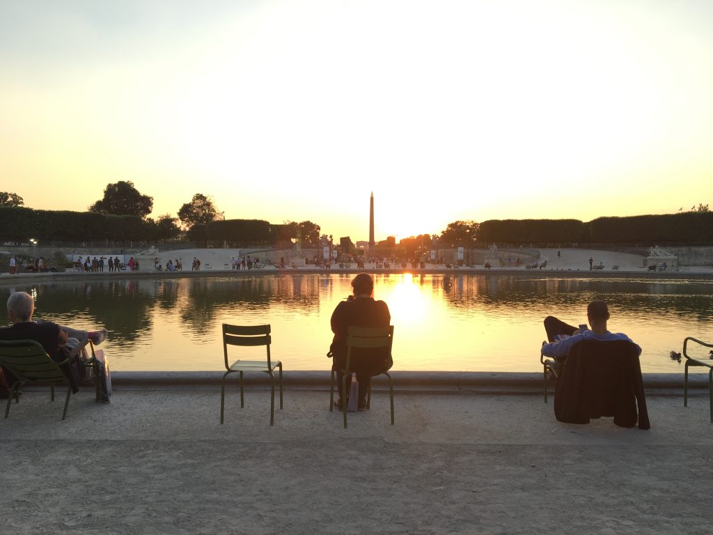 u efemme est assise sur une chaise au Jardin des Tuileries et regarde le coucher de soleil sur Paris