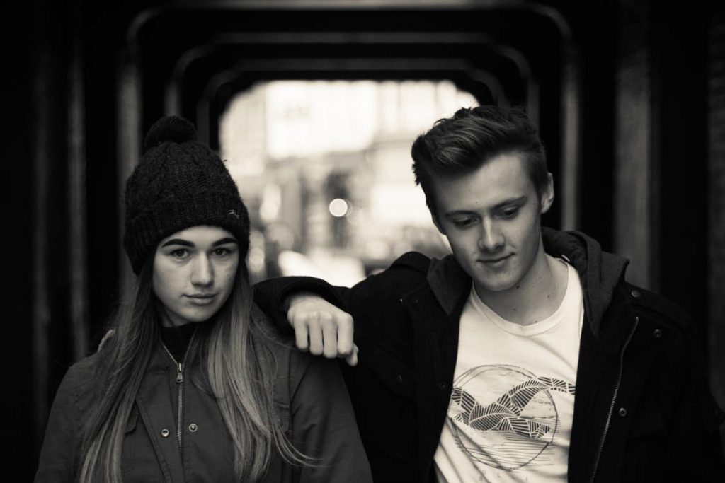 un jeune couple face à l'objectif, tous deux l'airun peu désabusé; La fille porte un bonnet, le garçon a le bras posé sur son épaule. La photo est en noir et blanc