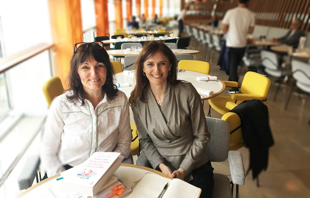 Caroline Webb et Marie-Laurence Cattoire après l'entretien, au café Radio Eat de la Maison de la Radio à Paris. Elle sosnt assises côte à côte et souris au photographe