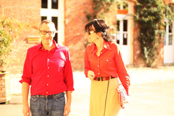 Un couple marche dans une cour ensoleillée. Ils sont tous deux vêtus d'une chemie rouge et ont l'air très heureux ensemble. La femme regarde vers l'homme.