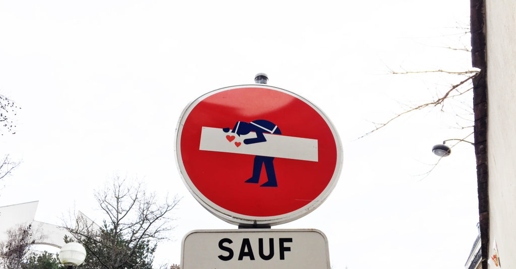 Dans la rue, un panneau de sens interdit est décoré d'un gendarme qui se penche sur la barre blanche pour l'embrasser. Un clin d'œil drôle et un bon remède à l'inquiétude !