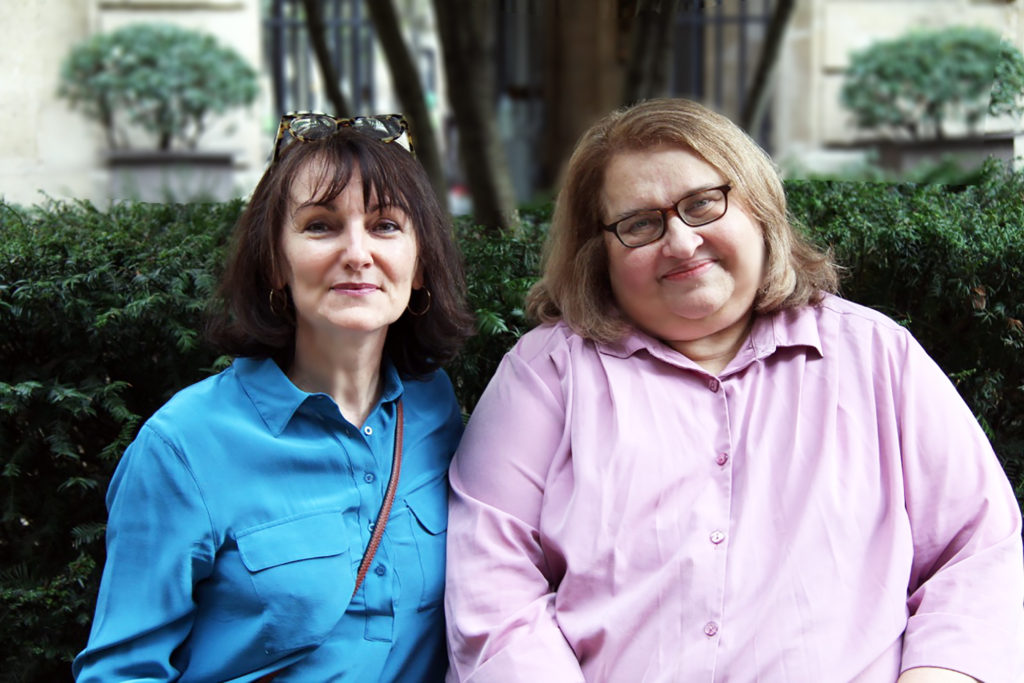 Marie-Laurence Cattoire, en chemisier bleu, et Sharon Salzberg, en chemisier rose, sont assises cote à cote et regardent l'objectif en souriant. Derrères elle, le jardin intérieur d'un hôtel parisien.