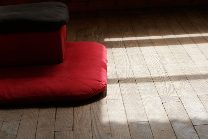 Un coussin de méditation posé sur un parquet en bois. Un rayon de soleil vient l'éclairer.