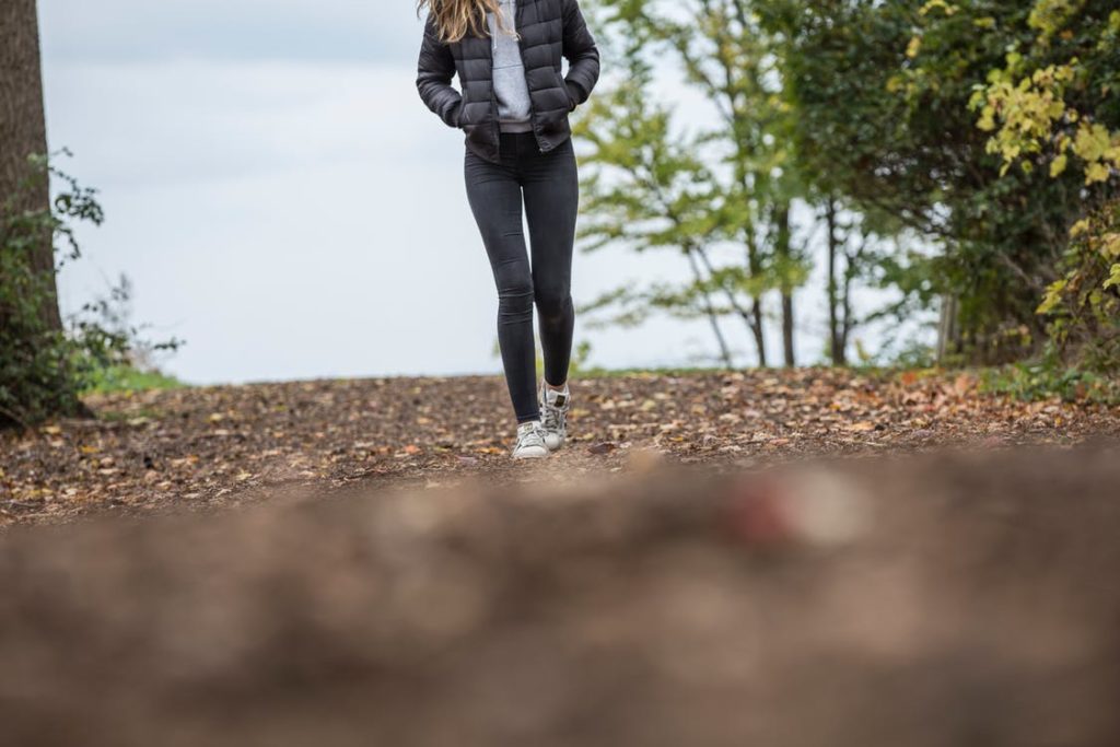 Une jeune femme marche dans la nature. On ne voit que ses jambes et son coprs, pas sa tête. Elle avance vers l'objectif les mains dans les pocheses