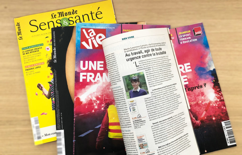 Sur un bureau en bois, une revue de presse où sont étalés les magazines Le Monde des Religions, Sens & Santé et La Vie ouvert à la page de l'itw de Marie-Laurence Cattoire