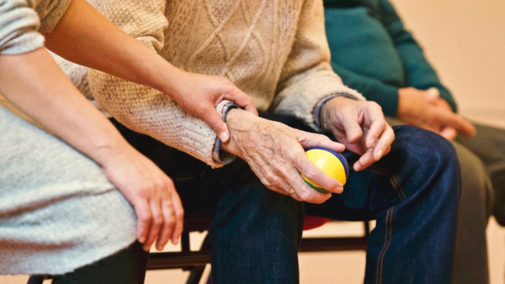 on voit le smains de personnes âgées assises sur un banc public. Une main de femme prend le poignet d'une main d'homme