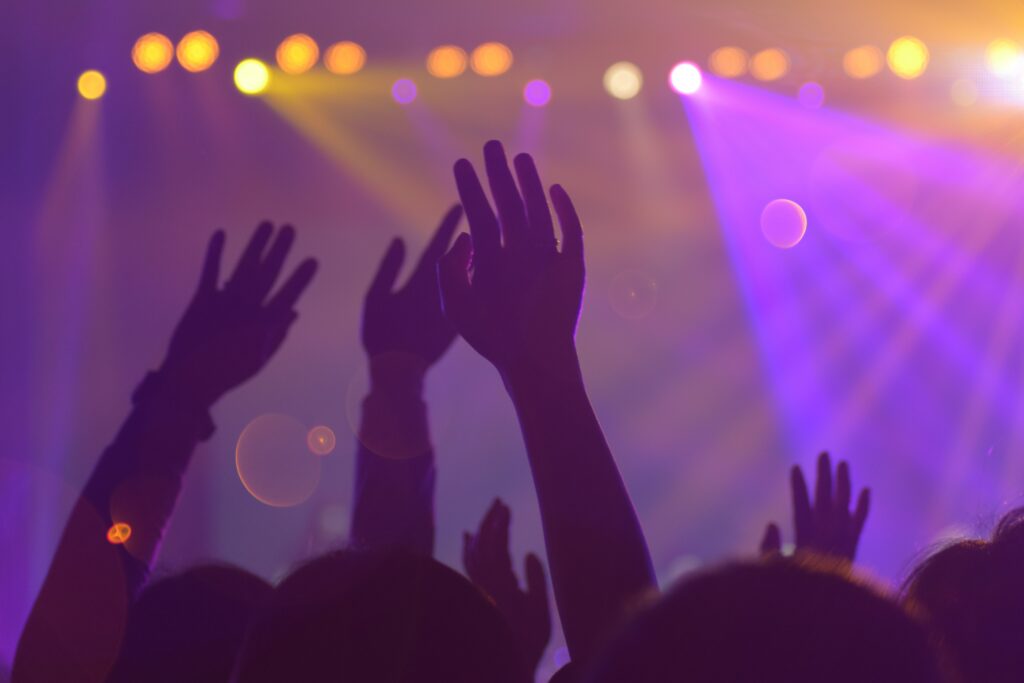 Des mains levées vers le ciel dans une salle de spectacle. Comme une danse joyeuse sous les lumières violettes et jaunes