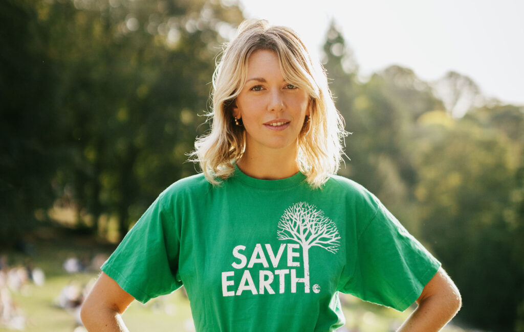 Lauren Bastide est face caméra, cheveux blonds, photographiée en pleine nature. Elle porte un tee-shirt vert sur lequel est inscrit "save earth"