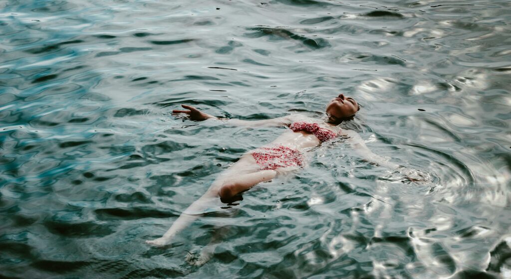 Une belle photo en couleur de Busranur Aydin d'une femme qui fait la planche dans l'océan. Elle porte un maillot de bain deux pièces rouge. La surface de l'eau scintille comme une métamorphose