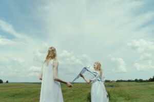 Deux femmes blondes en robe blanche qui se ressemblent symbolisent l'influence. Elles courent dans un pré avec un cerf-volant en mains. Une Photo du studio Cottonbro